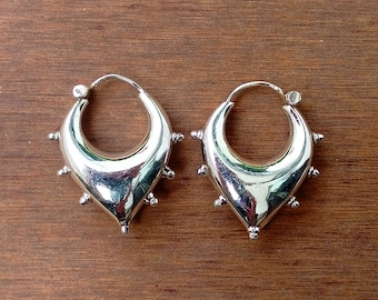 May include: A pair of silver hoop earrings with a unique design. The hoops are shaped like a crescent moon and have small, round studs around the edges.