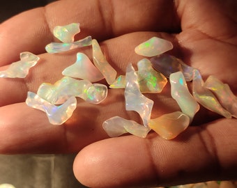 Puede incluir: Una colección de piedras preciosas de ópalo iridiscente en varias formas y tamaños. Los ópalos son una mezcla de blanco, rosa y verde.