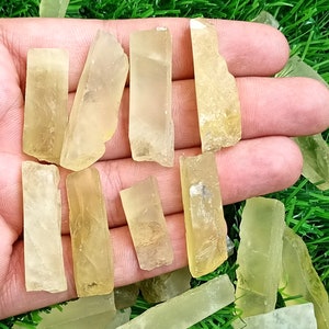Puede incluir: Una colecci&oacute;n de peque&ntilde;as puntas de cristal transl&uacute;cidas de color amarillo verdoso. Las puntas est&aacute;n dispuestas en una mano, con algunas de las puntas superpuestas.