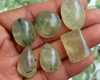 May include: Six green aventurine cabochons with black inclusions. The cabochons are in various shapes, including oval, round, pear, and rectangular.