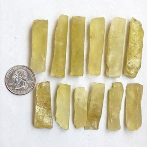 Puede incluir: Una colecci&oacute;n de 12 piezas de piedra preciosa amarillo-verde, cada una cortada en forma rectangular larga. Las piezas est&aacute;n dispuestas en dos filas sobre una superficie blanca. Una moneda de 1 euro se incluye para la escala.