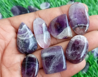 May include: Seven amethyst gemstone cabochons in various shapes and sizes, including oval, teardrop, and square, with purple and white banding.