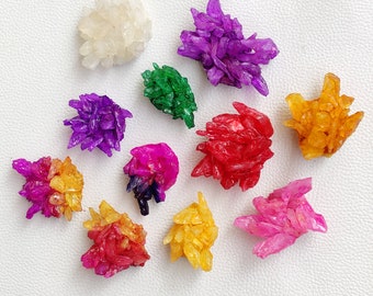 May include: Assortment of colorful crystal clusters in various shapes and sizes. The crystals are arranged on a white background. The colors include purple, red, orange, yellow, green, and white.