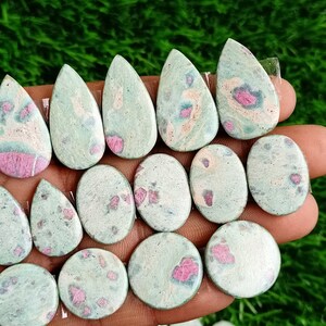 Könnte beinhalten: Eine Sammlung von grünen und rosafarbenen Edelstein-Cabochons in ovaler und tropfenförmiger Form. Die Steine haben eine marmorierte Optik mit rosa und weißen Einschlüssen.