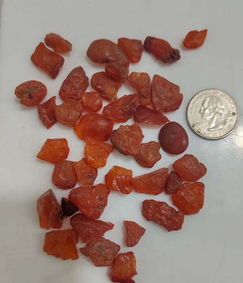 Op de afbeelding: Een verzameling van ongeveer 30 kleine, ruwe, rood-oranje barnsteenstenen. De stenen zijn van verschillende vormen en maten, sommige zijn ronder en andere hoekiger. Een Nederlandse 2-euro munt is opgenomen voor de schaal.