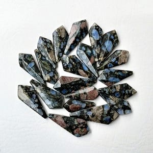 Könnte beinhalten: Eine Sammlung von 15 dunkelblauen, schwarzen und rosafarbenen Edelstein-Spitzen mit einem gesprenkelten Muster. Die Spitzen sind in einem Kreis auf einer weißen Oberfläche angeordnet.