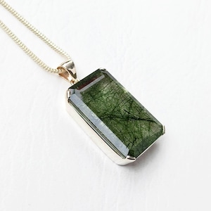 May include: A silver pendant necklace featuring a large, rectangular green gemstone with a unique, sparkly, and fibrous texture.