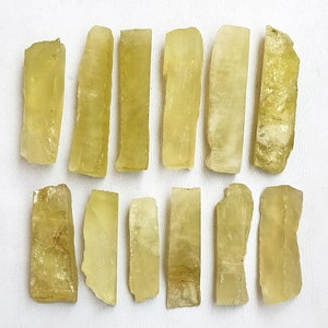 Puede incluir: Una colecci&oacute;n de 14 palitos de cristal de calcita de color amarillo verdoso. Los palitos son de varios tama&ntilde;os y formas, algunos son m&aacute;s redondeados y otros m&aacute;s angulares. Los cristales son transl&uacute;cidos y tienen un ligero brillo.