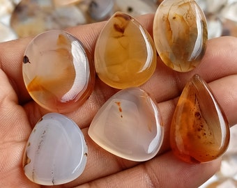 May include: Six agate gemstone cabochons in various shades of brown, orange, and white. The cabochons are teardrop shaped and have a smooth, polished finish.
