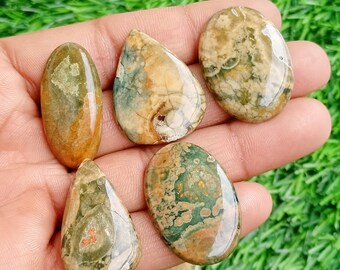 May include: Five polished, oval-shaped, green, brown, and white ocean jasper cabochons. The cabochons are smooth and have a variety of patterns.