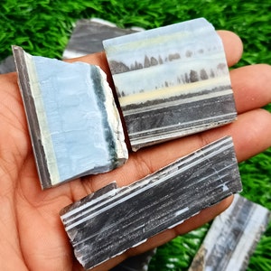 Könnte beinhalten: Eine Sammlung von drei Stücken gebänderten Achats mit verschiedenen Farben wie Schwarz, Weiß, Blau und Gelb. Der Achat ist poliert und hat eine glatte, glänzende Oberfläche.