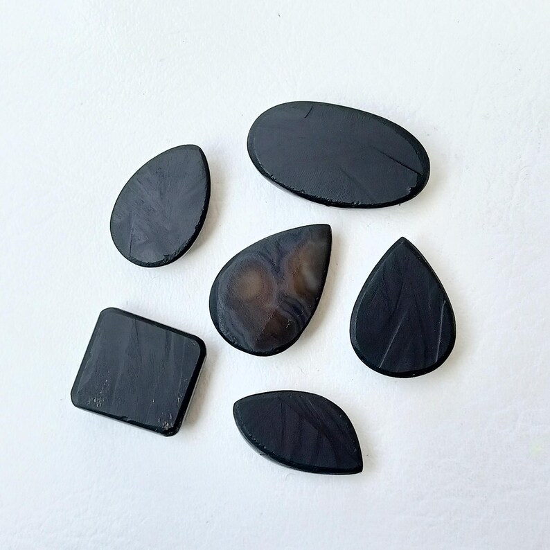 Op de afbeelding: Zes zwarte en bruine edelsteen cabochons in verschillende vormen, waaronder ovaal, druppelvormig en vierkant. De stenen hebben een gladde, gepolijste afwerking.