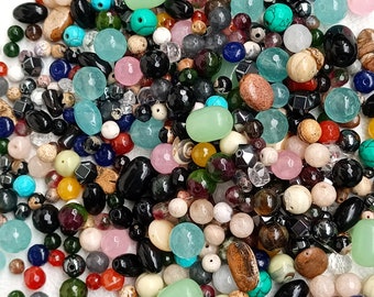 May include: A large assortment of colourful and natural gemstone beads, including turquoise, green, red, brown, black, and white beads. The beads are of various shapes and sizes, and some have a polished finish.