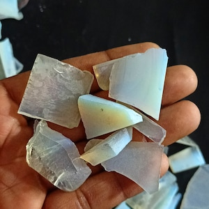 May include: A collection of iridescent opal gemstone chips in various shapes and sizes. The chips are translucent and have a milky white colour with flashes of rainbow hues.