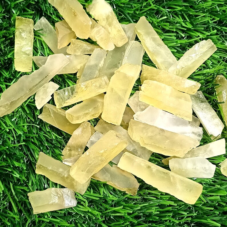Puede incluir: Una colecci&oacute;n de puntas de cristal de selenita amarilla transl&uacute;cida, tambi&eacute;n conocidas como spar satinado, dispuestas sobre una superficie de c&eacute;sped artificial verde.