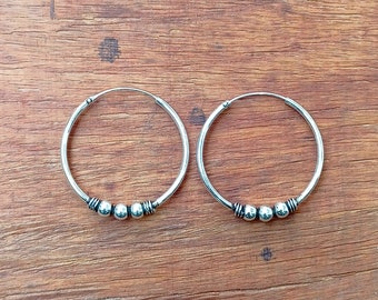 May include: A pair of silver hoop earrings with three small silver beads on each hoop.
