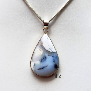 May include: A teardrop-shaped pendant with a silver chain. The pendant features a large, polished stone with a white, gray, and blue pattern. The stone is set in a silver bezel. The number "2" is visible in the lower right corner.