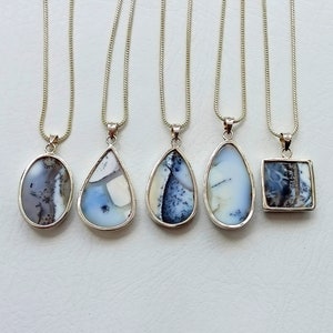 May include: Five silver pendant necklaces with different shaped natural stone pendants. The pendants have a mix of white, blue, and black patterns. Each pendant is on a thin silver chain.
