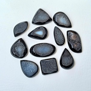 Op de afbeelding: Tien zwarte en grijze agaat cabochons met een kristal-achtig patroon. De cabochons zijn in verschillende vormen en maten.