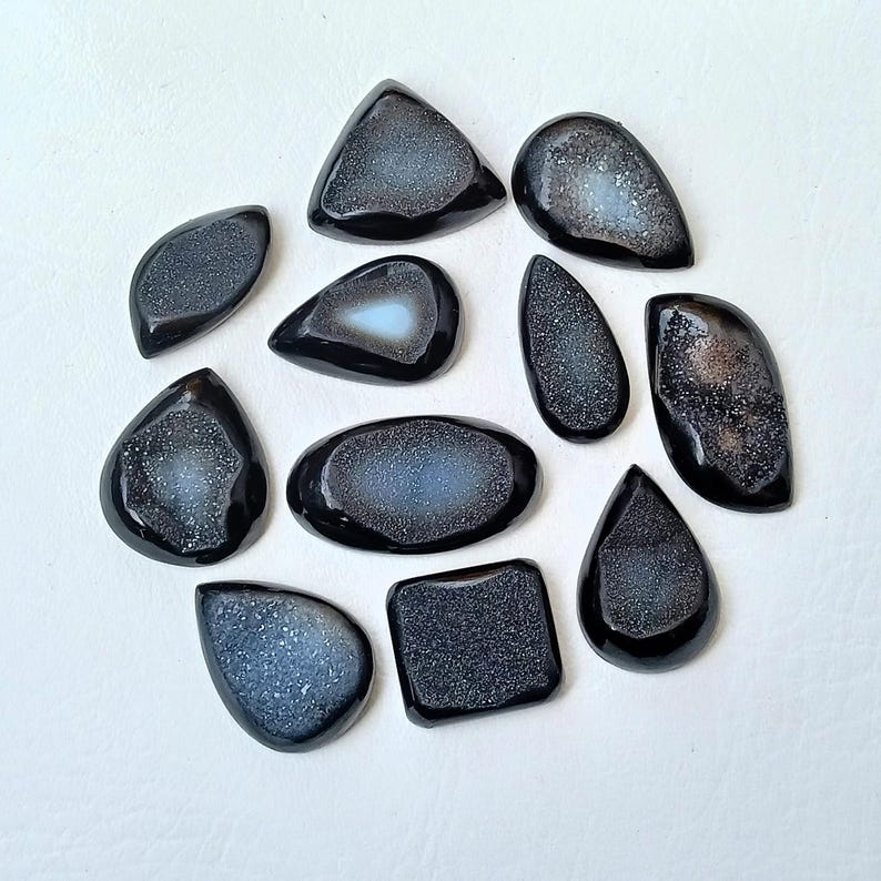 Op de afbeelding: Tien zwarte en grijze agaat cabochons met een kristal-achtig patroon. De cabochons zijn in verschillende vormen en maten.