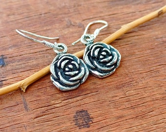 May include: A pair of silver rose earrings with a delicate design. The earrings are hanging from a wooden surface.
