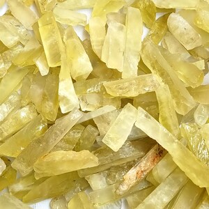 Puede incluir: Una colecci&oacute;n de puntas de cristal de calcita amarilla, tambi&eacute;n conocida como calcita lim&oacute;n, con una apariencia transl&uacute;cida. Los cristales son de varios tama&ntilde;os y formas, algunos tienen una punta m&aacute;s puntiaguda que otros.