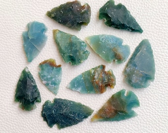 Puede incluir: Una colección de diez piedras en forma de punta de flecha de color verde y azul. Las piedras presentan una variedad de patrones y texturas.