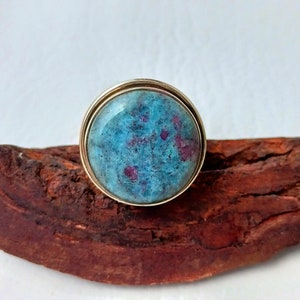 May include: A gold ring with a large, round, blue and pink gemstone set in a gold bezel.