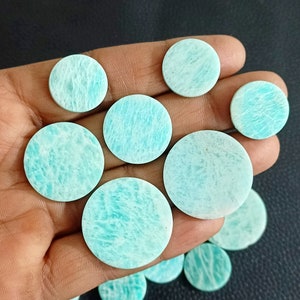 Könnte beinhalten: Eine Sammlung runder, glatter, hellblauer und grüner Amazonit-Cabochons in verschiedenen Größen. Die Cabochons sind in einer Hand angeordnet, wobei der größte Cabochon in der Mitte liegt.