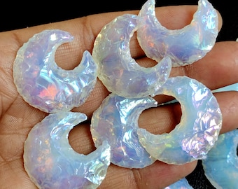 Op de afbeelding: Een verzameling van regenboogkleurige opalite halve maanvormige stenen. De stenen zijn melkachtig wit met een regenboogkleurige glans.