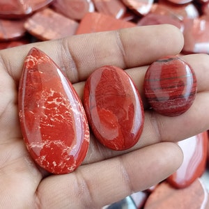 Puede incluir: Tres cabujones de piedra preciosa roja, uno en forma de lágrima, uno ovalado y uno redondo. Las piedras tienen un patrón de mármol rojo y blanco.