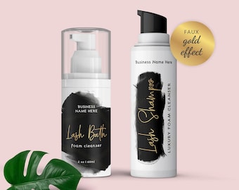 May include: Two white bottles with black brushstroke designs and gold lettering. The bottle on the left is labeled "Lash Bath foam cleanser" and the bottle on the right is labeled "Lash Shampoo LUXURY FOAM CLEANSER". The bottles are on a pink background with a green leaf.