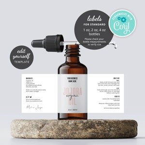 May include: A brown glass bottle with a dropper filled with jojoba oil. The label is white with pink text that says "Jojoba Organic Oil" and has a business name placeholder. The label also includes ingredients, how to use, and benefits. The bottle is sitting on a brown stone surface.