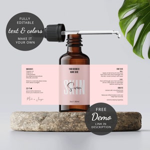 May include: A brown glass bottle with a dropper filled with a clear liquid. The bottle has a pink label with the text "Skin Serum" and "Your Business Name Here". The label also includes ingredients, instructions for use, and benefits. The bottle is sitting on a stone surface with a green leaf in the background.