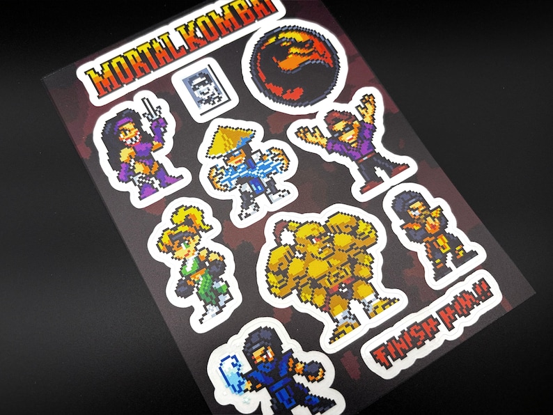 May include: A sheet of Mortal Kombat stickers featuring pixelated character designs. The stickers include characters in various poses, with the Mortal Kombat logo and the phrase "FINISH HIM!!" in red and white.