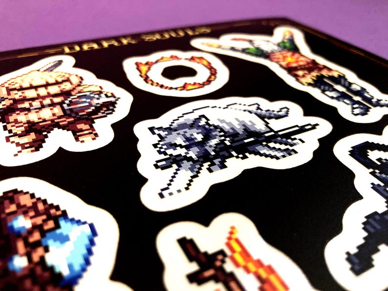 May include: A set of eight Dark Souls themed stickers featuring pixelated characters and objects from the video game. The stickers are printed on white paper and have a black background.