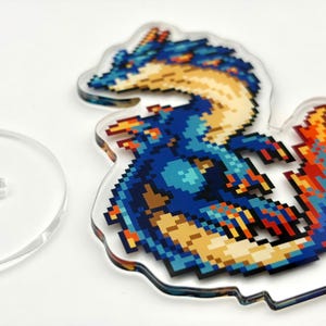 May include: A pixelated dragon design in shades of blue, yellow, and orange, on a clear acrylic stand. The dragon is detailed with a retro video game aesthetic. A separate clear acrylic stand is also visible.