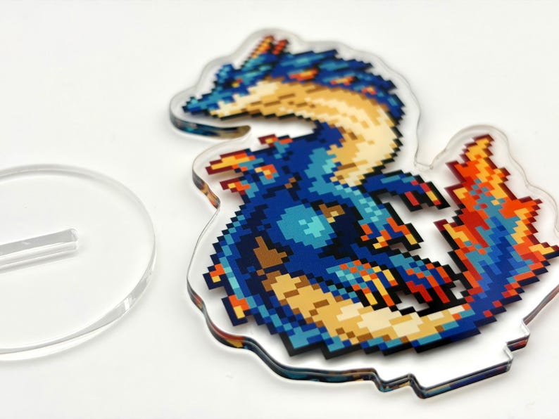 May include: A pixelated dragon design in shades of blue, yellow, and orange, on a clear acrylic stand. The dragon is detailed with a retro video game aesthetic. A separate clear acrylic stand is also visible.