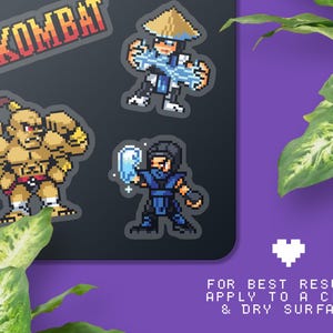 May include: Pixel art stickers featuring characters from Mortal Kombat. The stickers include a large red and orange Mortal Kombat logo, and pixelated images of three characters in various action poses. The text at the bottom says "FOR BEST RESULTS APPLY TO A CLEAN & DRY SURFACE."
