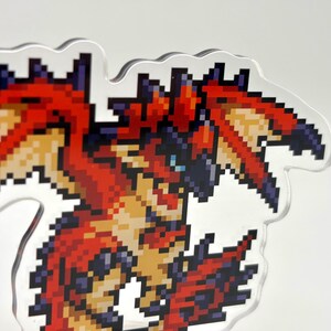 May include: A pixelated dragon design in red, orange, and blue. The dragon has a detailed, angular appearance with a clear, wavy outline. The artwork is reminiscent of classic video game graphics.