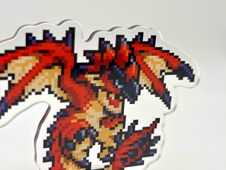 May include: A pixelated dragon design in red, orange, and blue. The dragon has a detailed, angular appearance with a clear, wavy outline. The artwork is reminiscent of classic video game graphics.