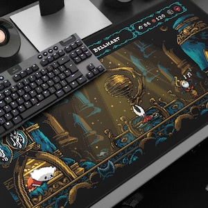 以下が含まれることがあります： ビデオゲームHollow Knightのピクセルアートが特徴の黒いゲーミングマウスパッド。マウスパッドには、キャラクターや建築要素を含むシーンの詳細なイラストが描かれています。黒いキーボードが上に置かれています。