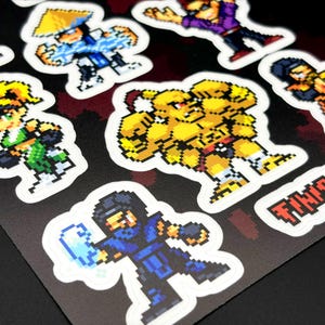May include: Sheet of pixel art stickers featuring various video game characters in action poses. The stickers are colorful with a white border and are on a black background. The text "FINISH HIM" is visible.