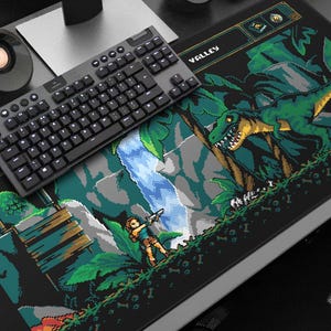 May include: Black gaming mouse mat with a pixelated jungle scene featuring a dinosaur and a character with a gun. A black keyboard sits on top of the mat. The word "VALLEY" is visible on the mat.
