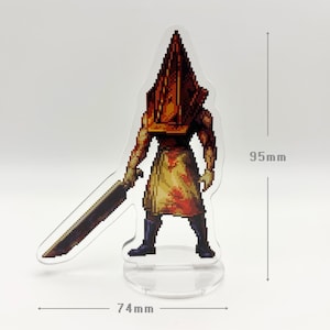May include: A clear acrylic stand-up figure of a pixelated character with a pyramid-shaped head and a large sword. The figure is 95mm tall and 74mm wide. The character is wearing a blood-stained apron.