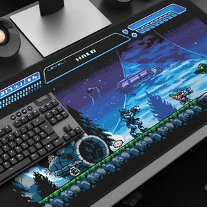 Könnte beinhalten: Eine schwarze Gaming-Tastatur und ein Mauspad mit Pixelkunst aus dem Videospiel Halo. Das Mauspad zeigt eine Szene mit Charakteren, einem Raumschiff und dem Wort "HALO". Die Tastatur ist schwarz mit grauen Tasten.