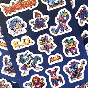 May include: A sticker sheet featuring pixel art characters from Darkstalkers, including Felicia, Demitri, and Morrigan. The sheet includes various colorful figures, a small bat, and the text R.O. in yellow pixelated letters against a dark blue background.