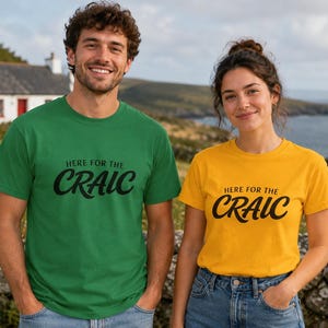 May include: Two people wearing matching t-shirts with the text "HERE FOR THE CRAIC" in black script. One shirt is green, the other is yellow. Both are short-sleeved and made of a soft material.