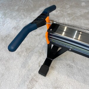 May include: A Concept2 Model D indoor rowing machine. It has a dark blue handle, orange details, and a silver metal rail. The frame is black, and the machine is designed for indoor exercise and fitness.