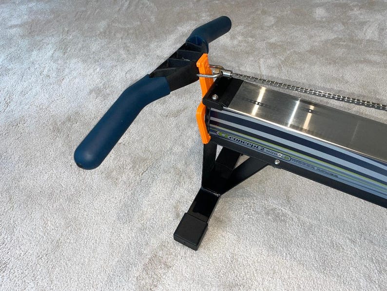 May include: A Concept2 Model D indoor rowing machine. It has a dark blue handle, orange details, and a silver metal rail. The frame is black, and the machine is designed for indoor exercise and fitness.